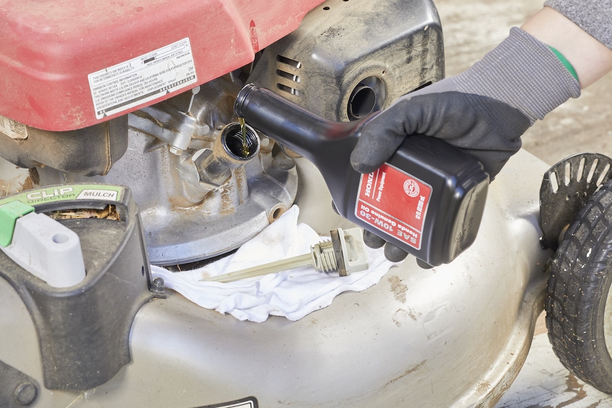 Person pours oil from a bottle into a lawn mower.
