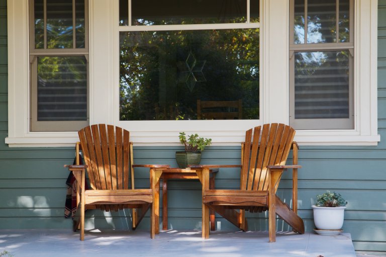 Two Adirondack chairs on a front porch of a house.