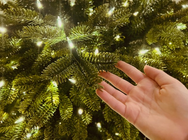 A person touching the molded, lifelike needles on the best prelit artificial Christmas tree.