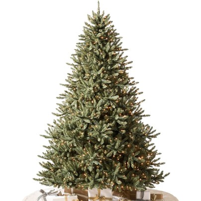 The Balsam Hill Prelit Classic Blue Spruce Christmas Tree on a white background with a beige tree skirt and several wrapped presents.