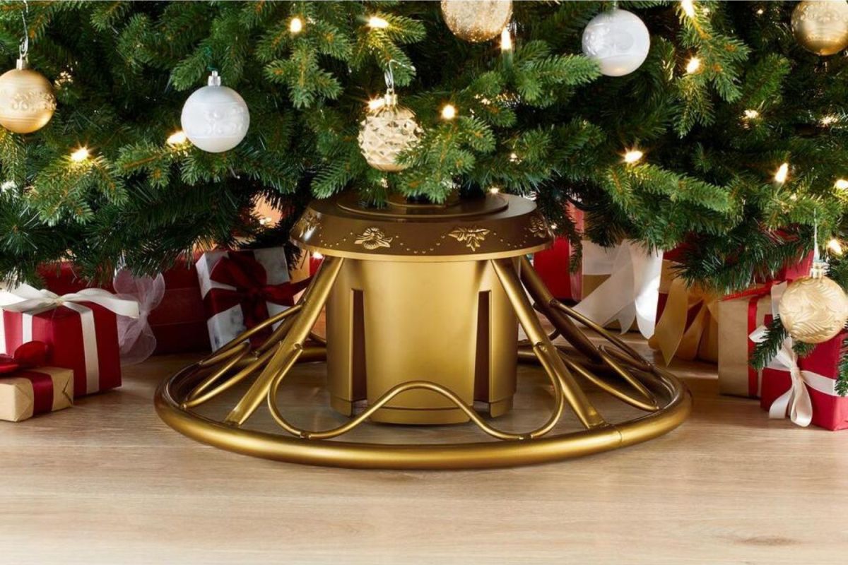 Gold rotating Christmas tree stand supporting artificial tree with white and gold ornaments