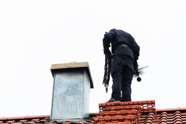 A worker dressed in black stands on a red tile roof.