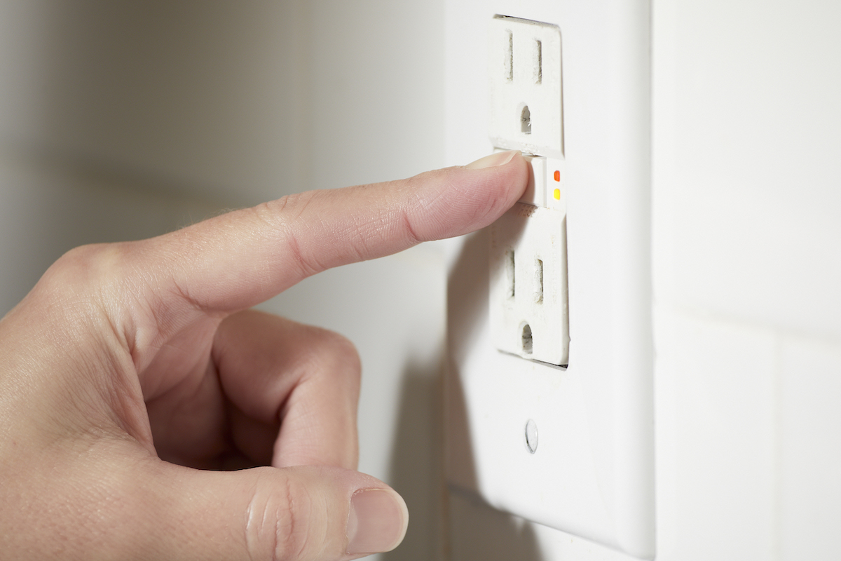 Woman pushes the test and reset buttons on a GFCI outlet.