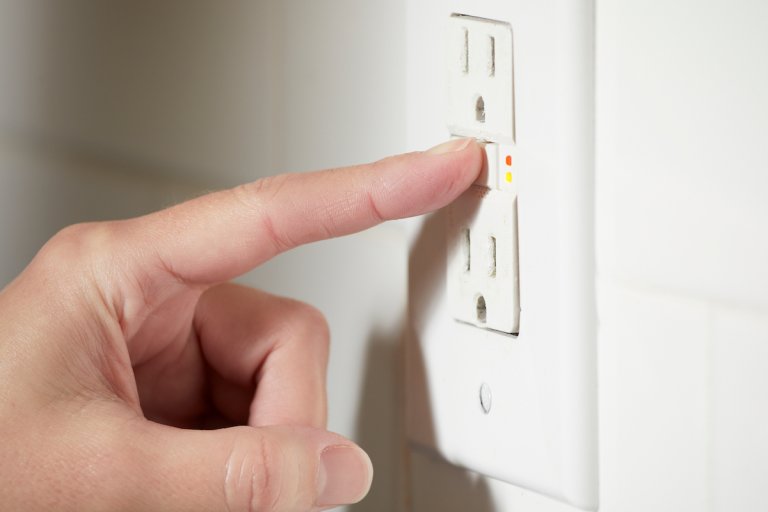 Woman pushes the test and reset buttons on a GFCI outlet.