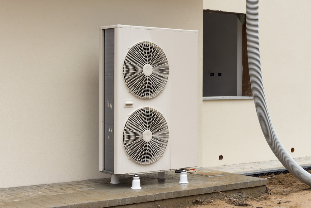 A heat pump installed on a beige exterior wall. 