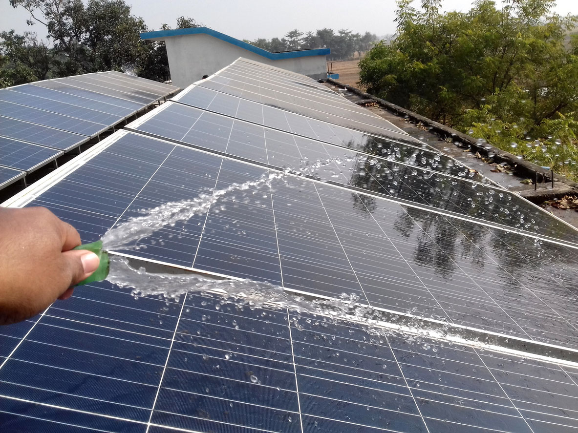 Person aims water from a garden hose at solar panels.