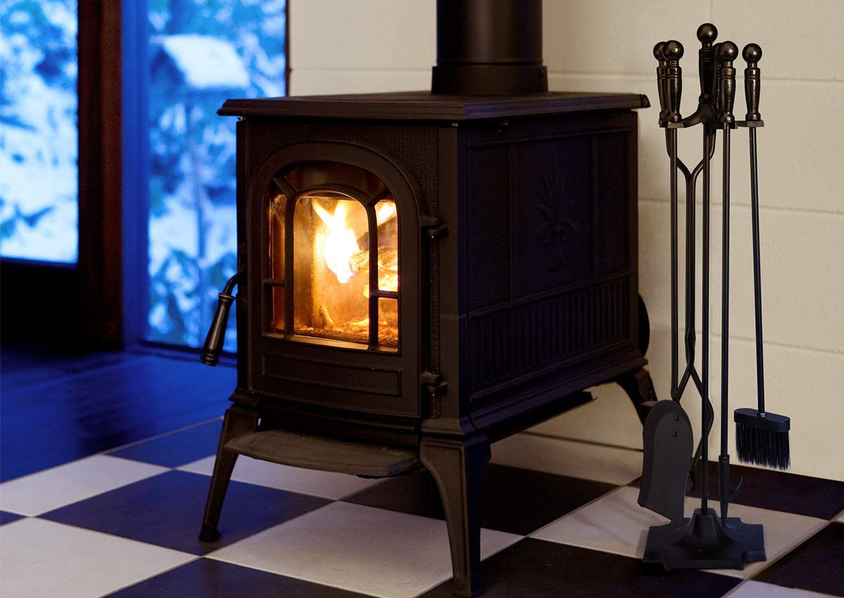 A set of the best fireplace tools next to a small wood-burning stove that's burning a fire.