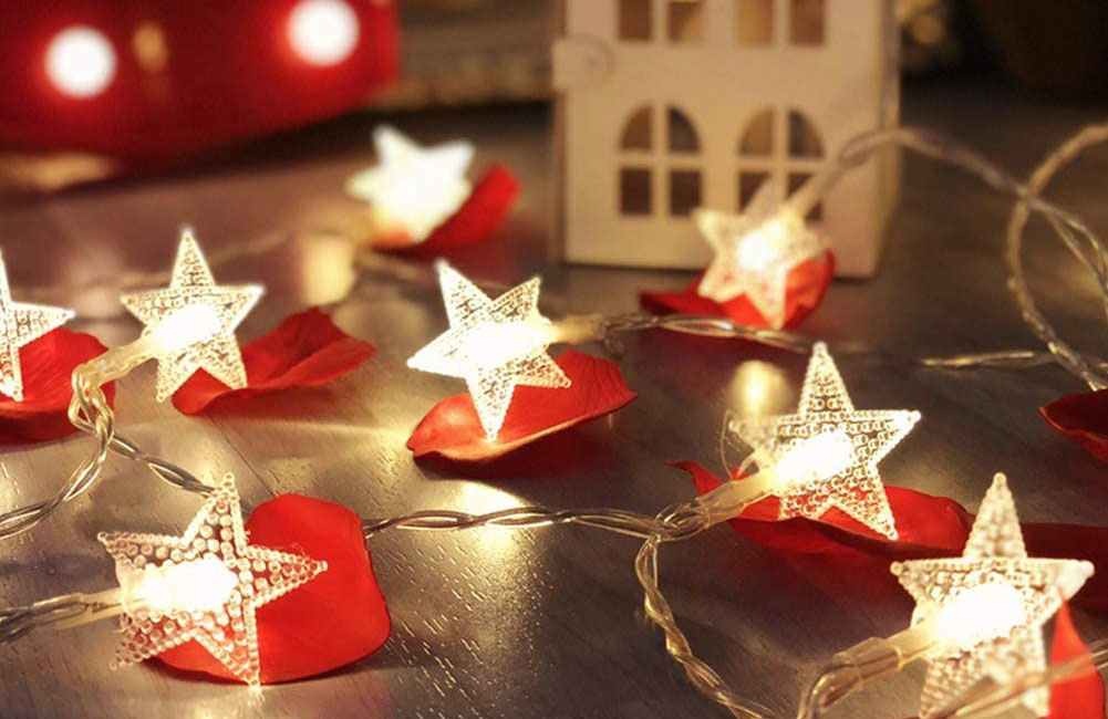 The Twinkle Star 100 LED Star String Lights arranged on a table next to red hearts and a small decorative house.