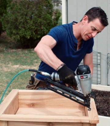A man uses a finish nailer on a wood project outside.