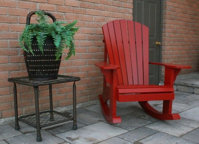Red Adirondack rocking chair next to patio table with plant