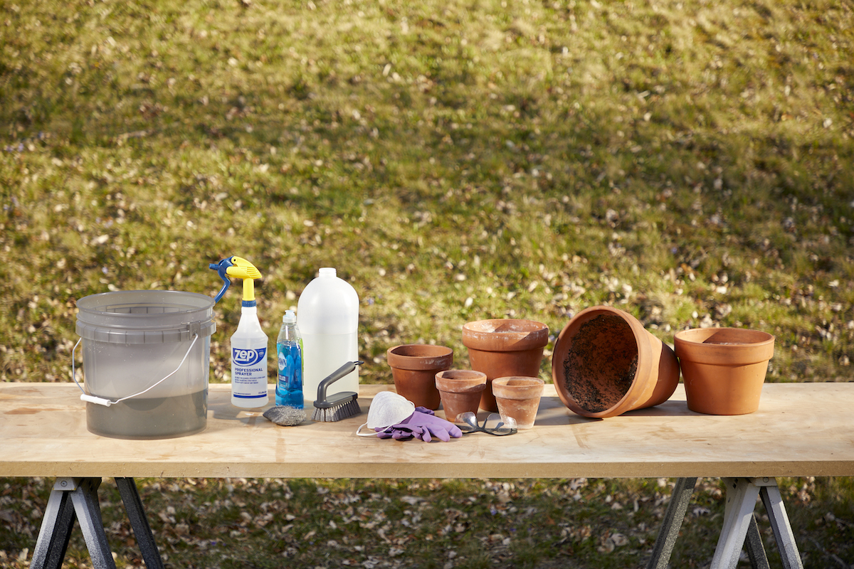 Terra-cotta pots on a table with materials used to clean them: vinegar, cleaning supplies, and bucket.