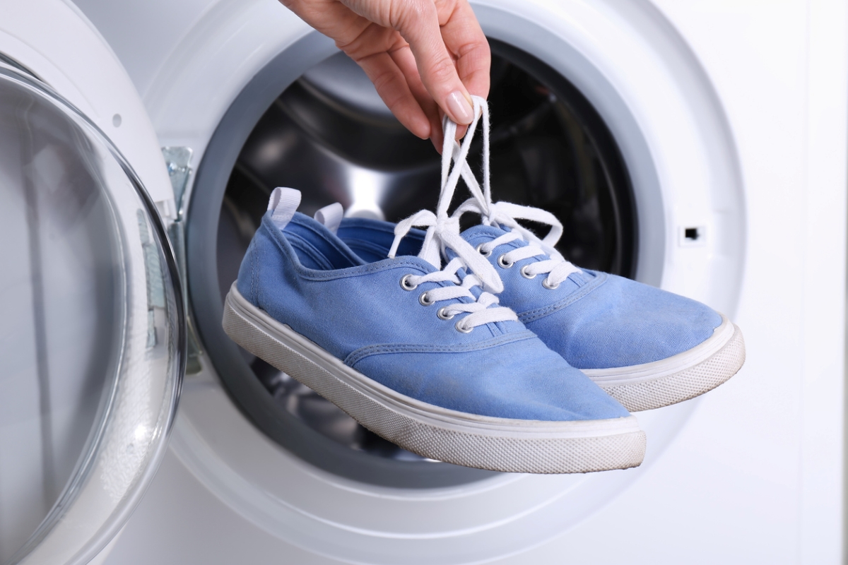 Person holding blue shoes in front of washer.