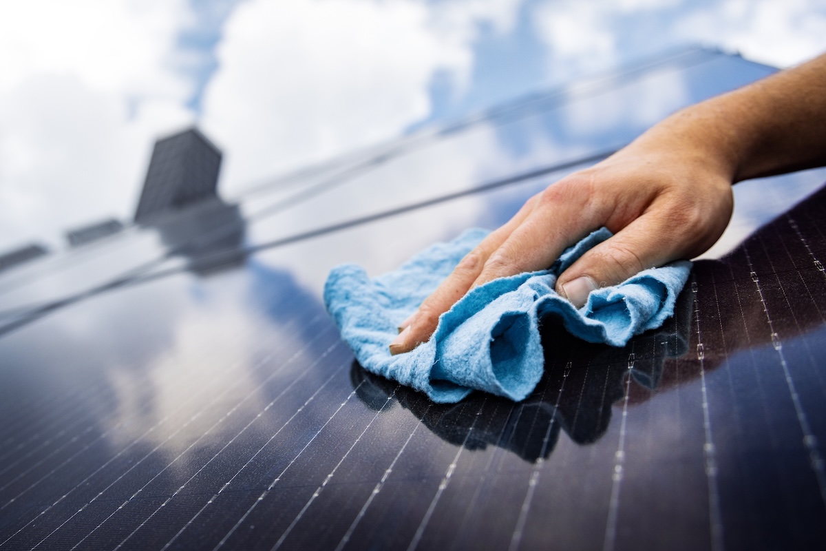 Close up of person wiping solar panels with a blue microfiber cloth.