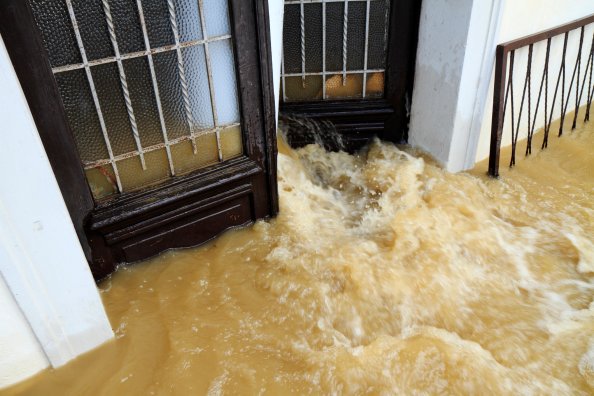 Muddy water pouring through a home's front door during a flood