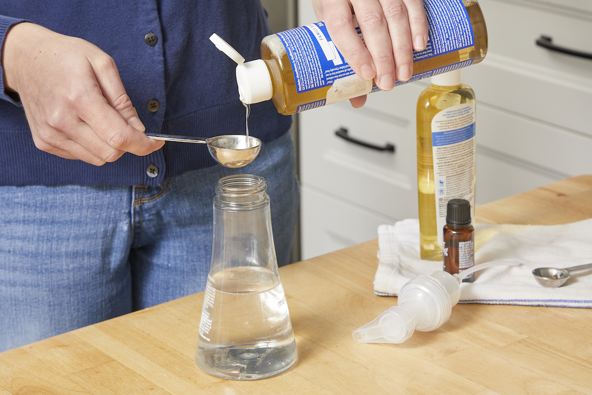 Woman making foaming hand soap adds castile soap to the bottle.
