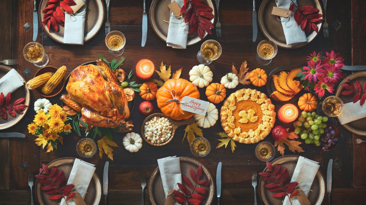 Thanksgiving dinner set tablescape with turkey, pumpkin centerpieces, and set place settings.