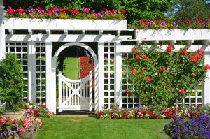 A large white ornamental garden gate and fence, surrounded by flowers.