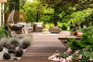 A wooden terrace surrounded by greenery, with wicker patio furniture and ornamental grasses.
