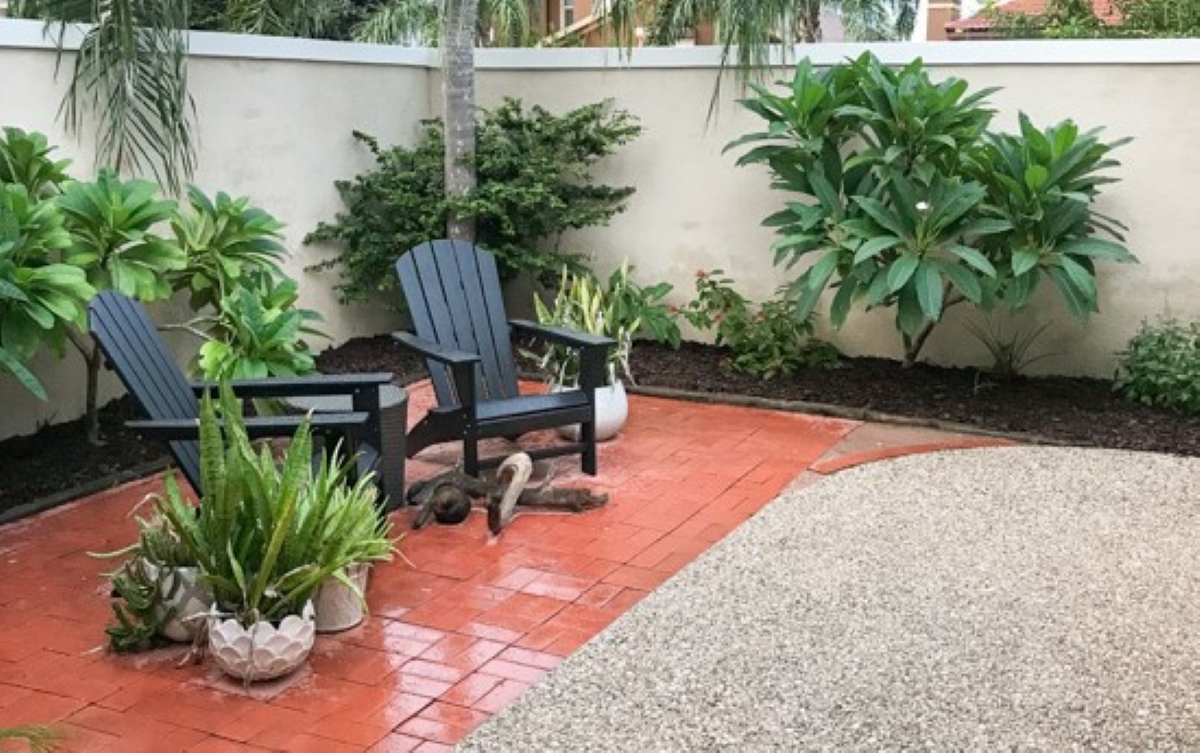 Two lawn chairs on brick patio next to stone covered area.