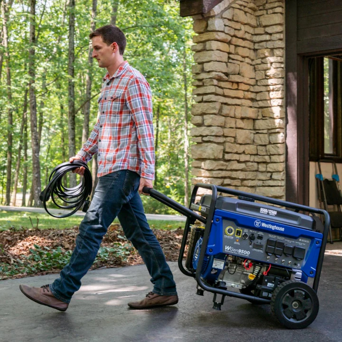 A man is rolling a portable generator outside with an extension cord in his hand.
