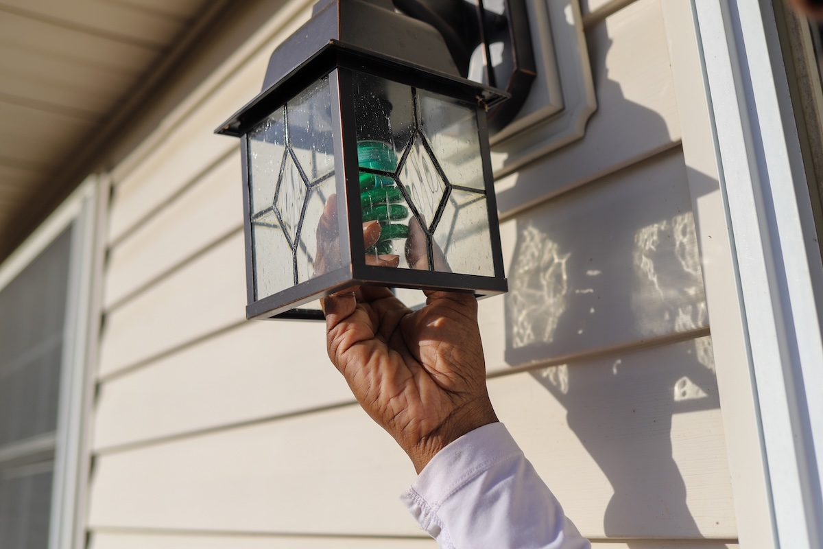 A homeowner installing a green light bulb in an outdoor porch light fixture.