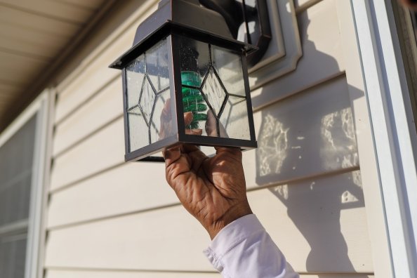 A homeowner installing a green light bulb in an outdoor porch light fixture.