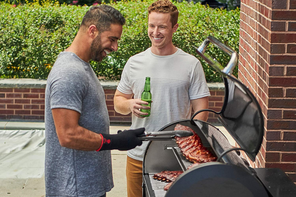 A grillmaster and friend standing over the best pellet grill option while cooking steaks
