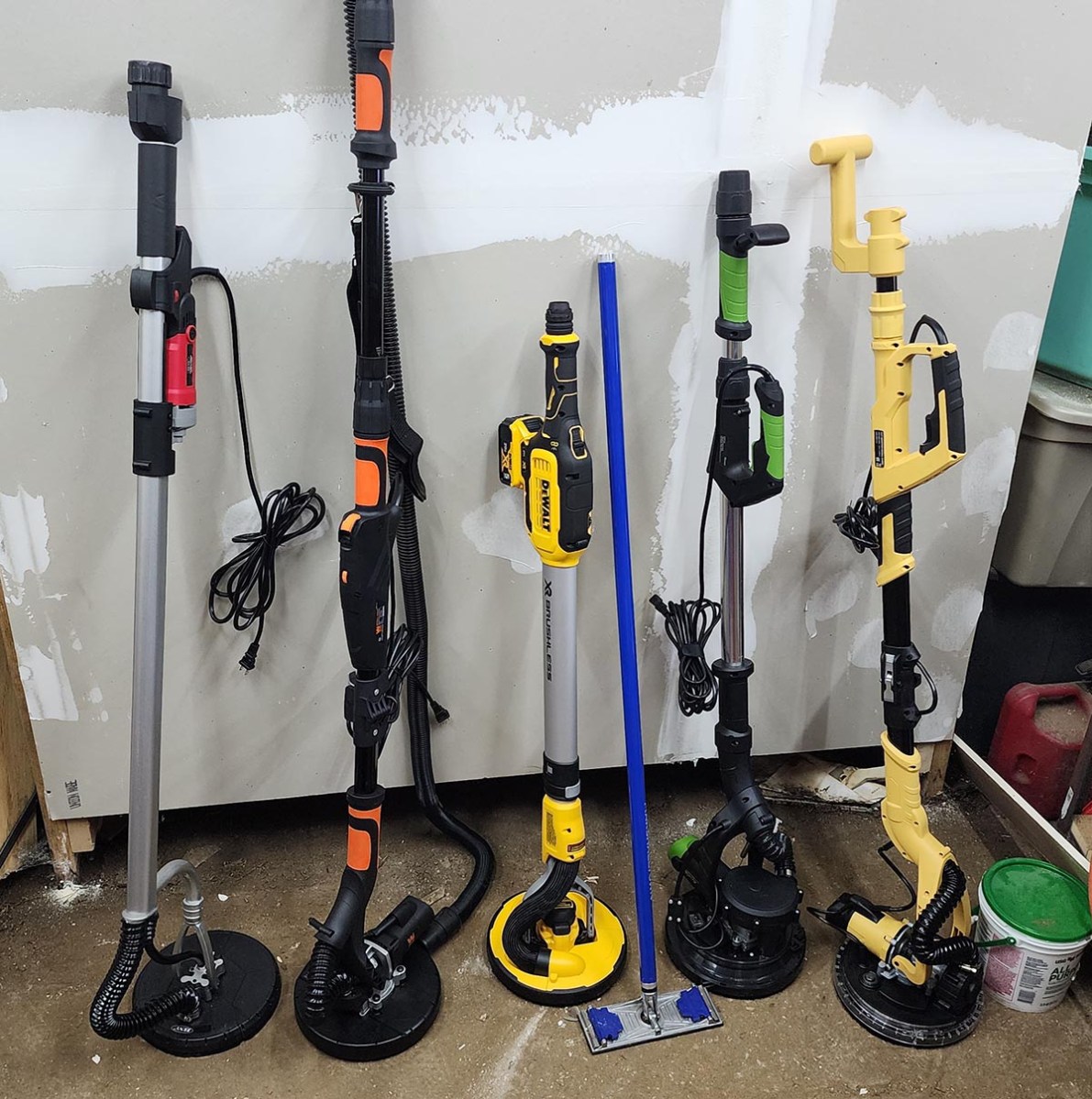 A group of the best drywall sander options together in front of a large section of drywall