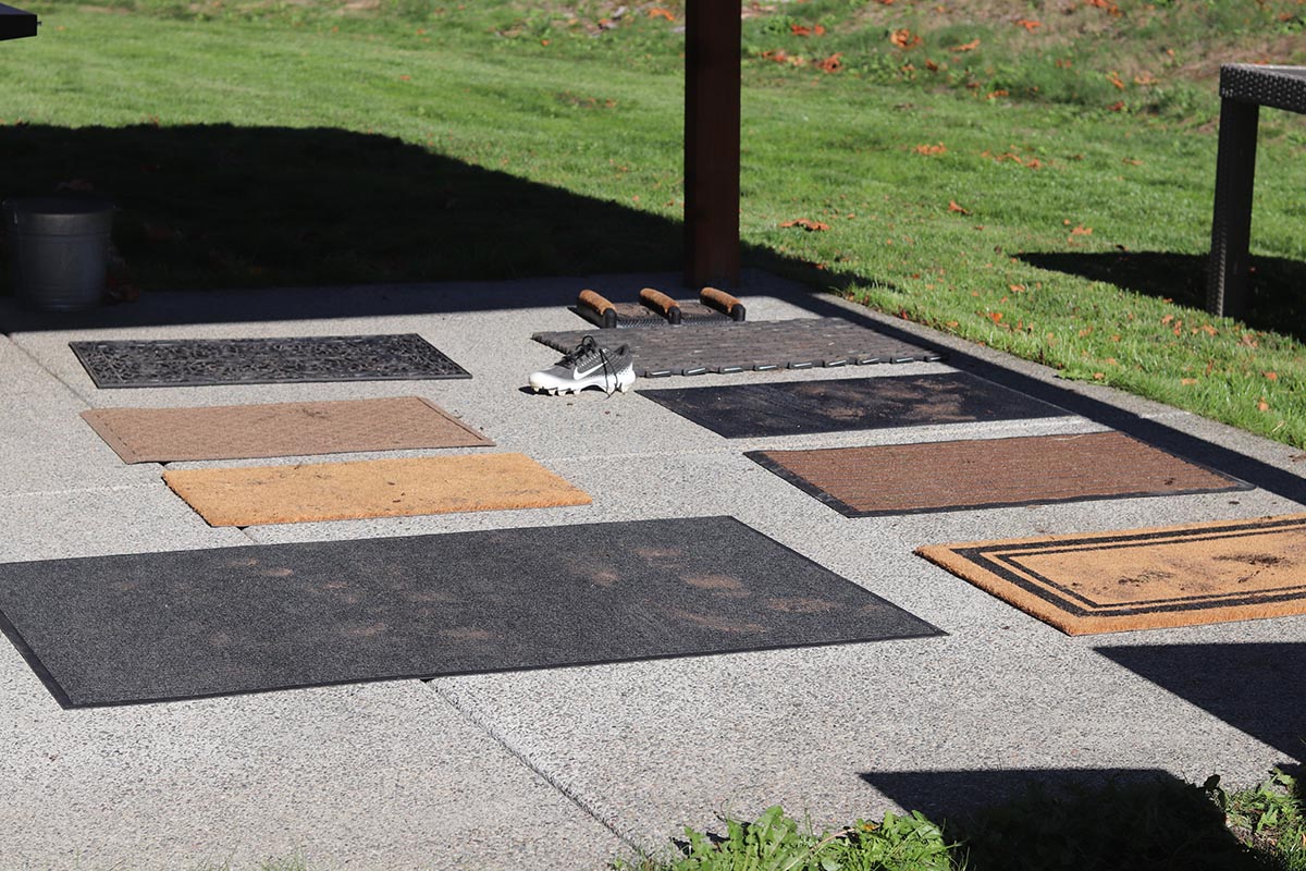 Collection of nine doormats drying in the sun on concrete patio