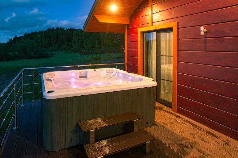 An illuminated hot tub on a deck at night is filled with water.