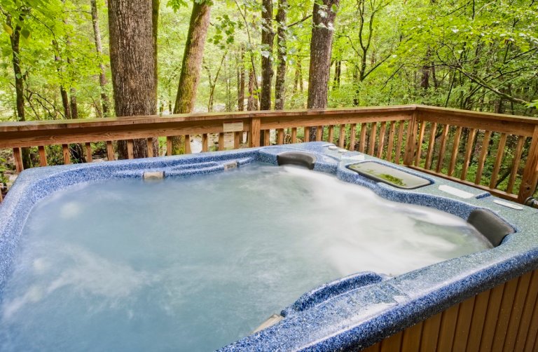 Full hot tub on the deck of a wood cabin, with verdant trees in the background.