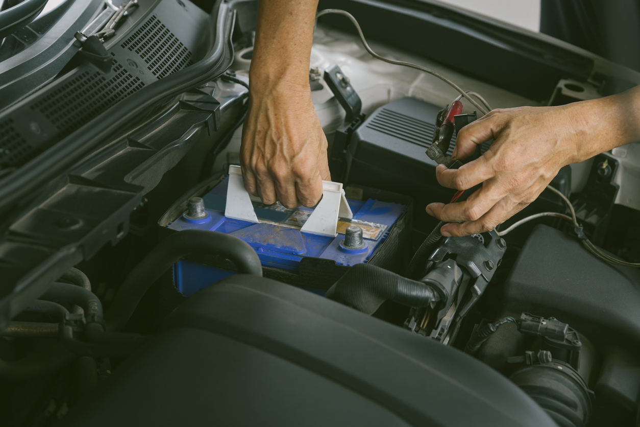 how to change a car battery mechanics hands pulling car battery out of engine