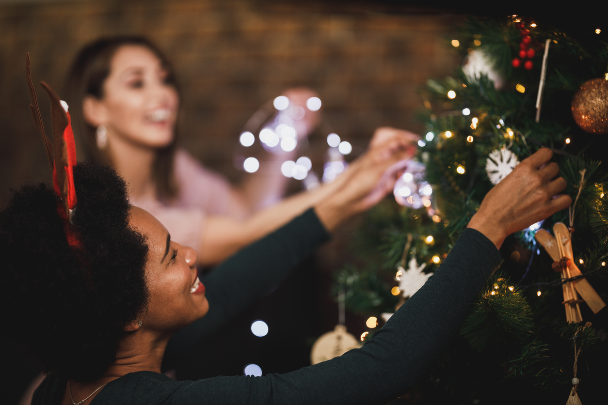 Happy African American woman enjoying holiday time at home, decorating her Christmas tree and arranging the christmas lights with friends.