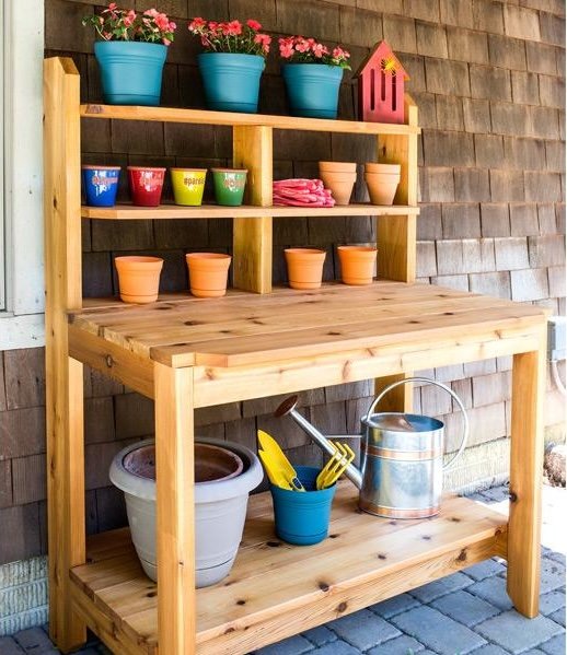 Photo of a cedar potting bench, shelves lined with colorful flower pots, against a wood-shingled house.