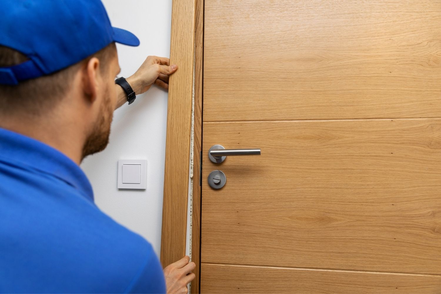 A worker in a blue shirt uses a blue shirt to finish installing a door. 