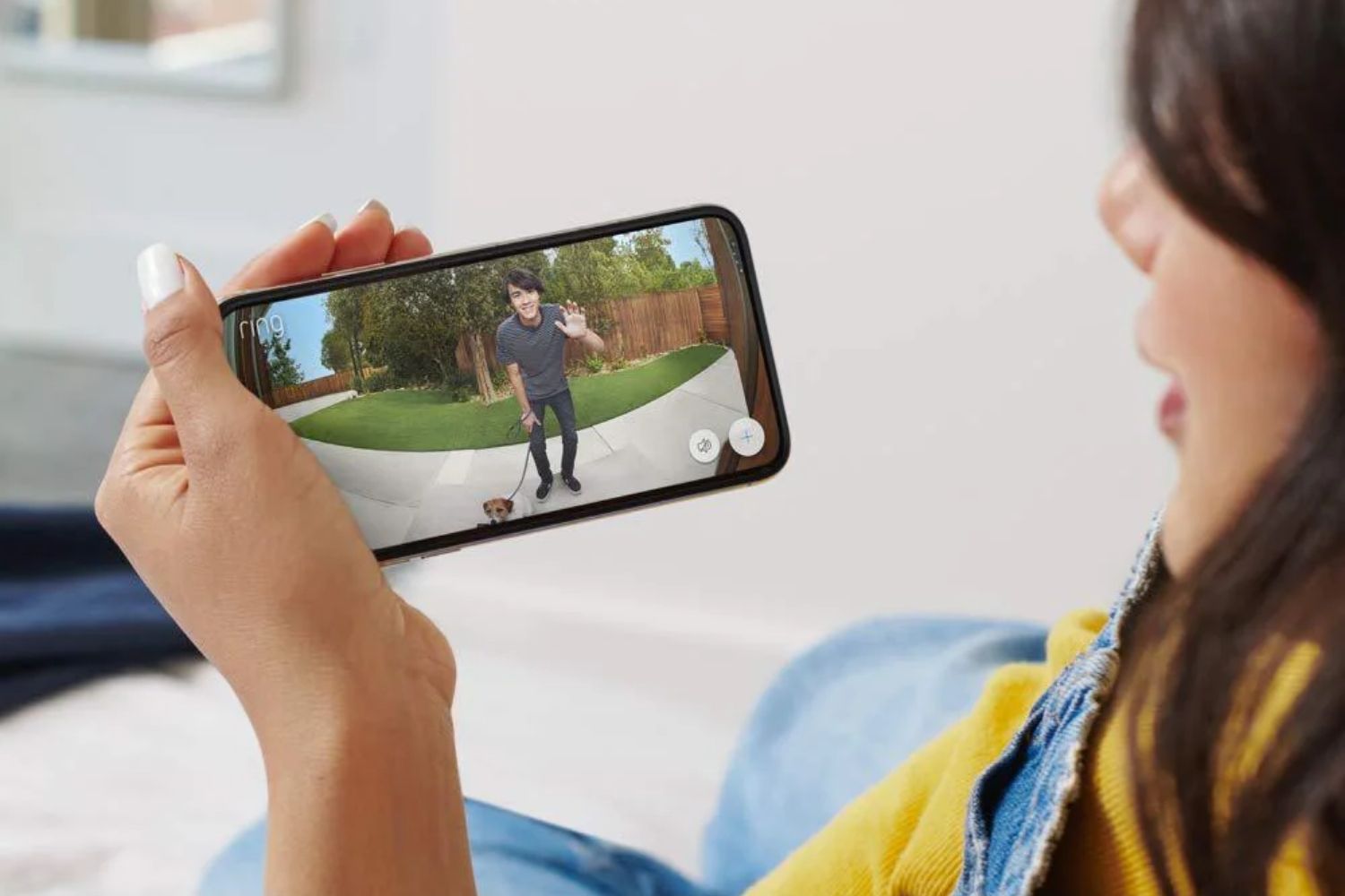 A person looking at the screen of the best home intercom system showing another person waving hello while walking a dog