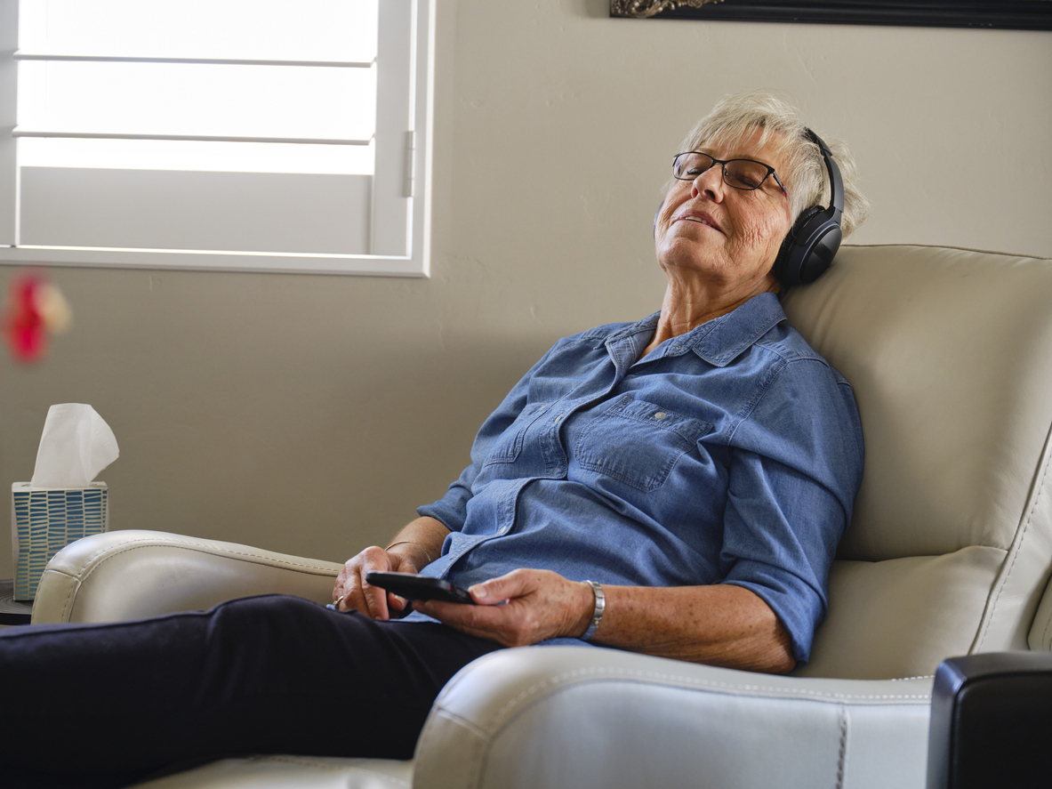 An older woman in the best recliner for sleeping option reclined with eyes closed and listening to headphones