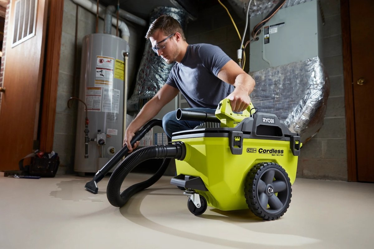 A man is using a compact shop vac to clean up water in the basement.
