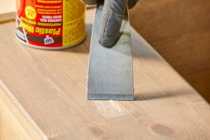 Woman uses a putty knife to apply wood filler to a nick in a wood board.