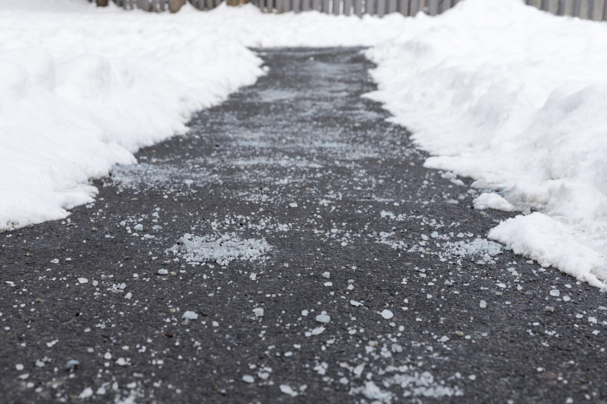 A driveway with ice melt residue down the middle and piles of snow on either side.