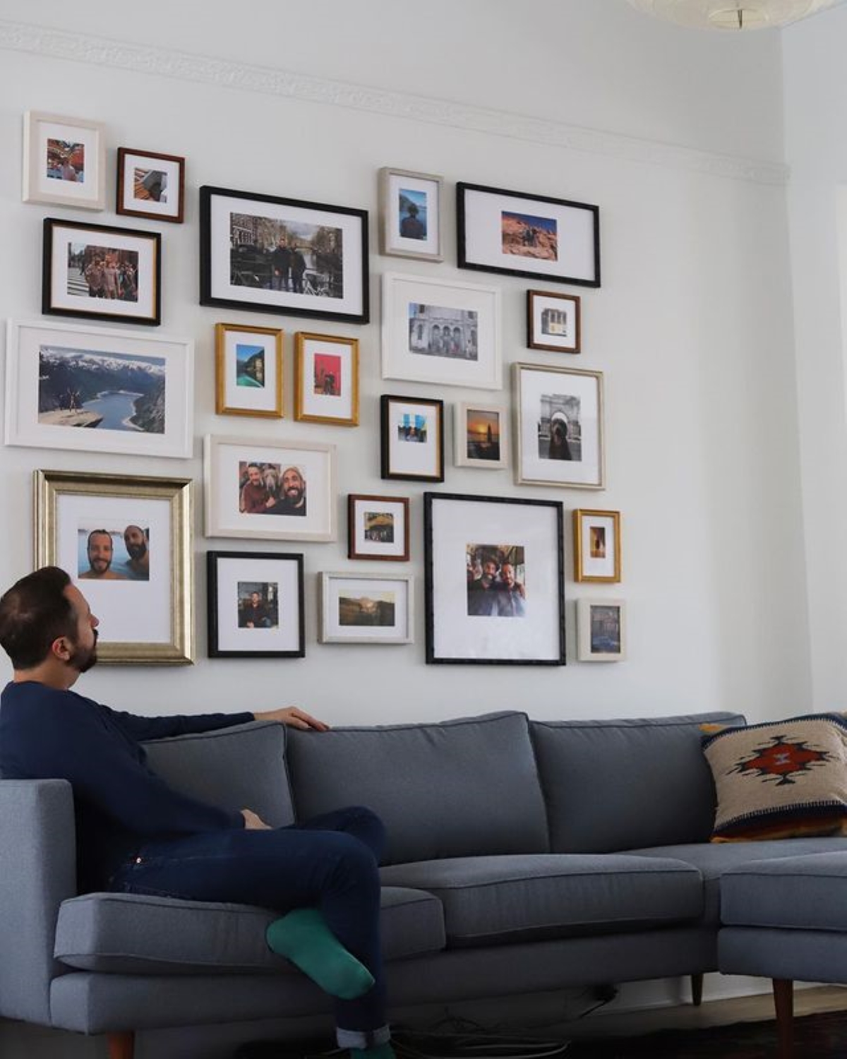 Man sitting on couch looking at photo gallery wall.