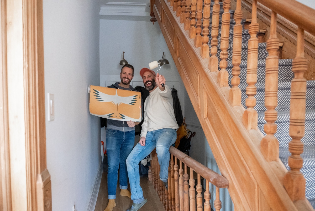 Two male designers holding wallpaper and paint roller.