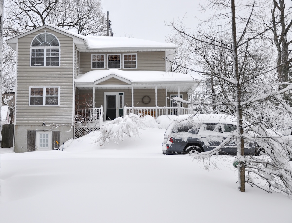 Snow covered two-story suburban home and car after a snowstorm. Not plowed.