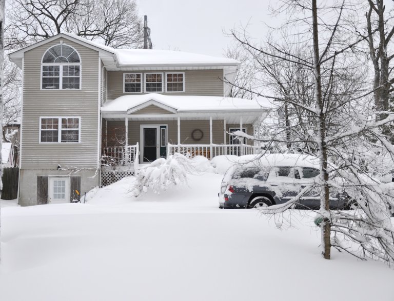 Snow covered two-story suburban home and car after a snowstorm. Not plowed.