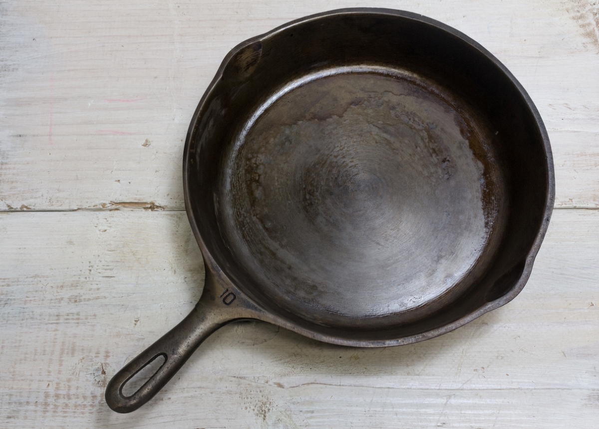 An unseasoned cast iron skillet on a whitewashed wooden table.