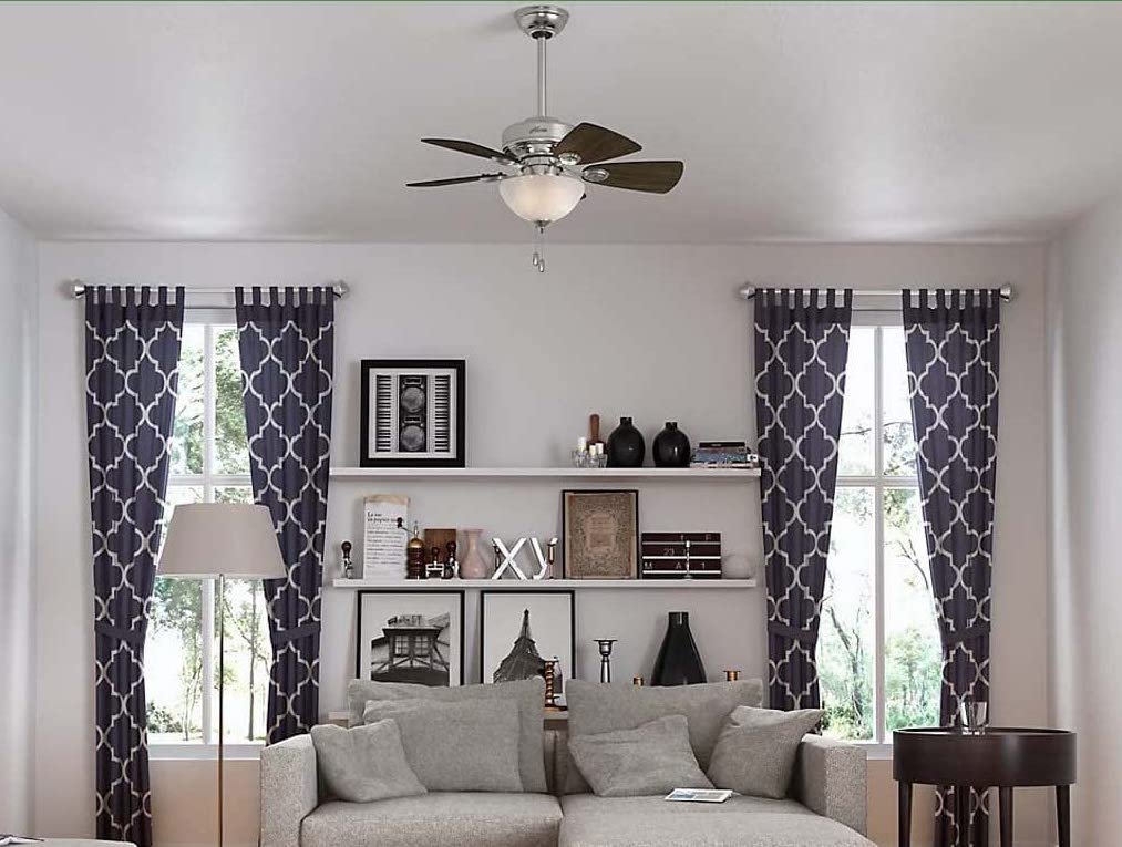 View of living area with ceiling fan, light grey couch and grey curtains.