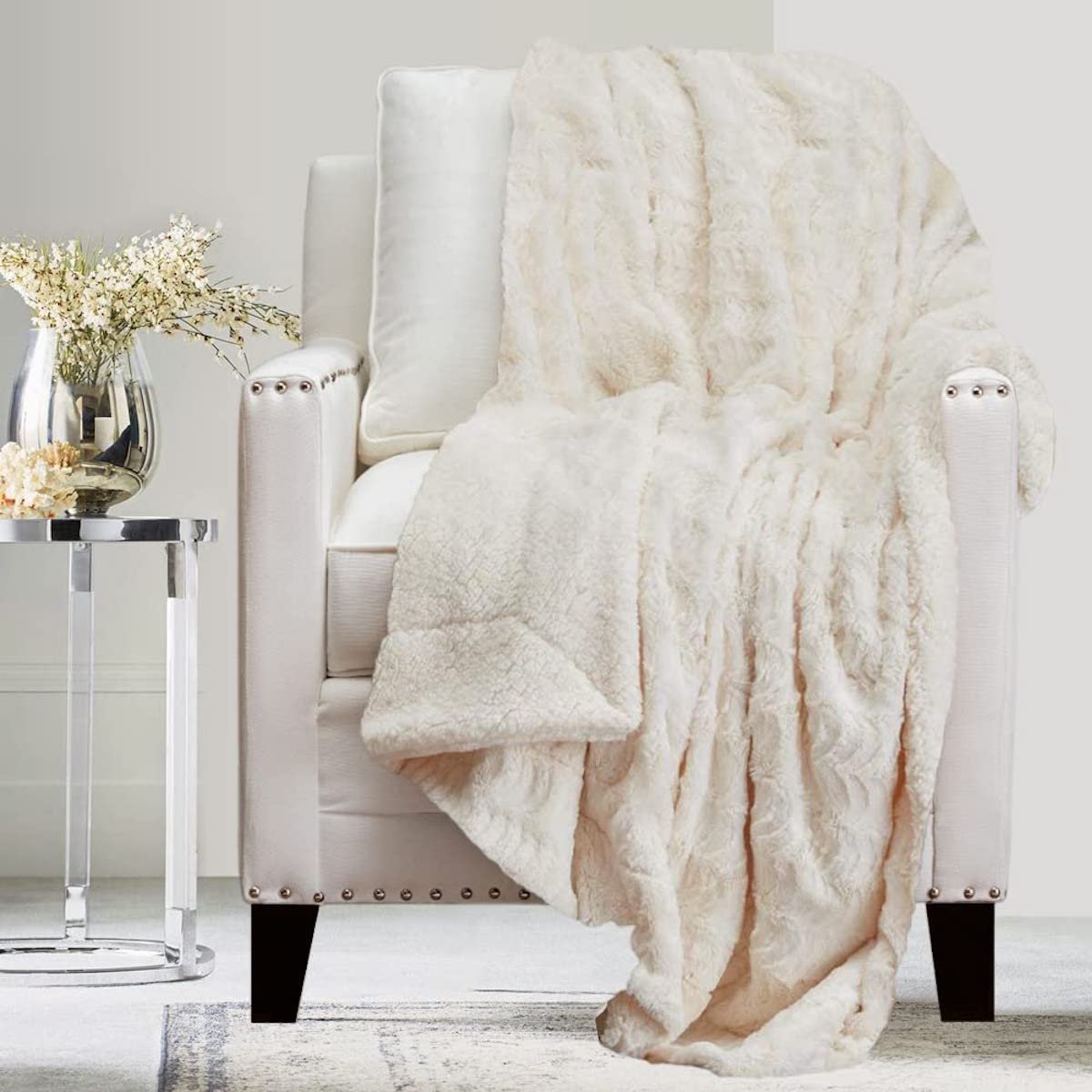 Luxe-looking white living room focusing on a white chair with a fluffy white throw blanket over top.