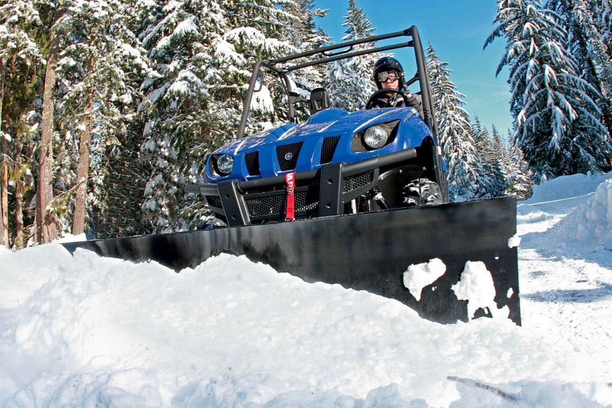 Man Using One Of The Best ATV Snow Plow Blades to Clear A Path Through A Snowy Landscape.