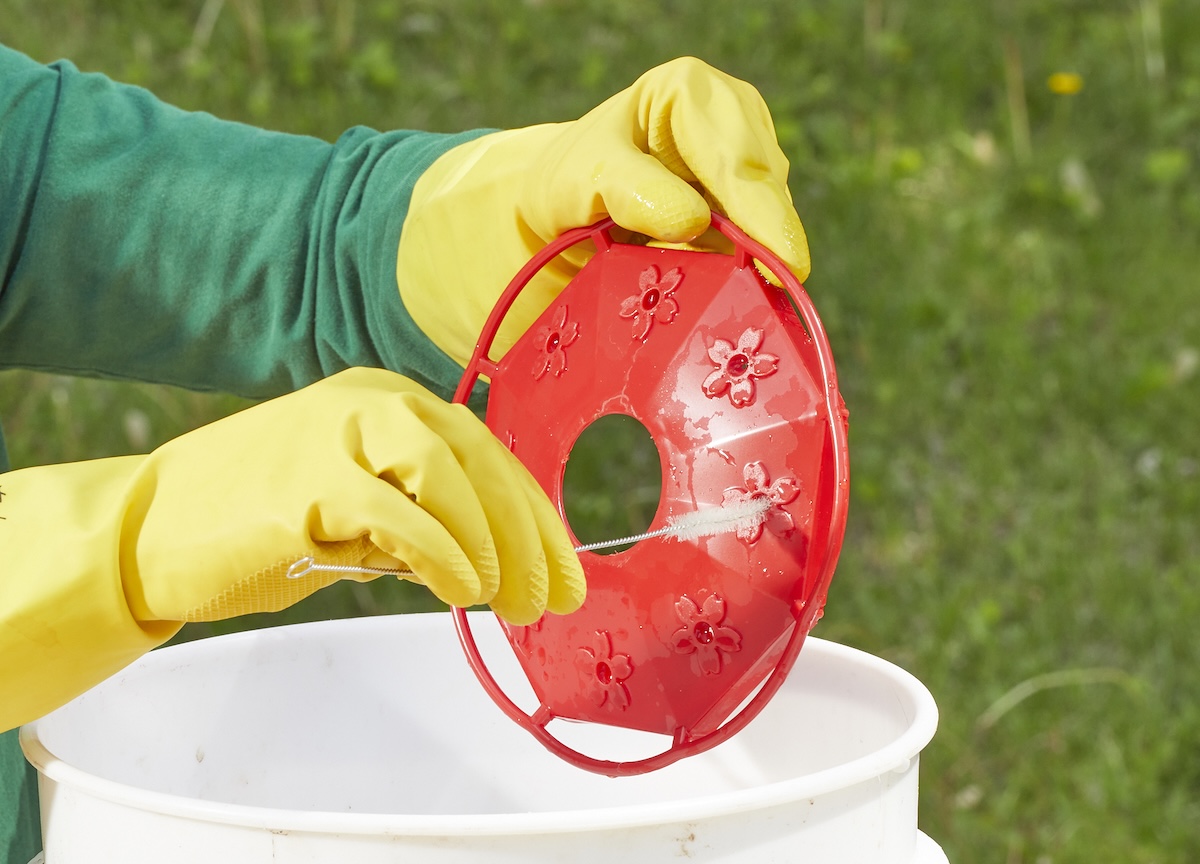 Person wearing yellow rubber gloves cleans ports on a hummingbird feeder.