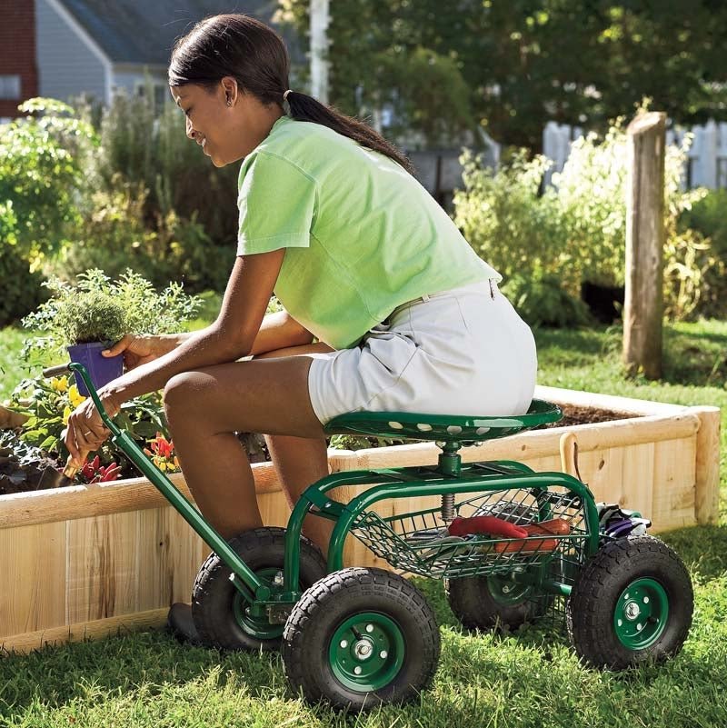 Woman sitting on a garden cart, reaching into a raised bed.